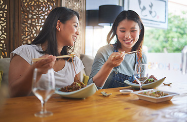 Image showing Restaurant, girl friends and lunch with food, noodles and cafe happy from bonding. Asian women, eating and plate together with friendship smile at a table hungry with chopsticks at Japanese bar