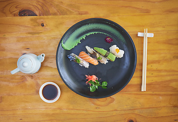 Image showing Sushi, food and chopsticks in an asian restaurant from above for fine dining or traditional cuisine. Salmon, menu and seafood with a chinese dish on a table in a local eatery for hunger or nutrition