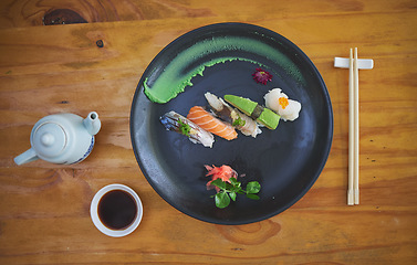 Image showing Sushi, seafood and chopsticks in a chinese restaurant from above for fine dining or traditional cuisine. Salmon, menu and food with an asian dish on a table in a local eatery for hunger or nutrition