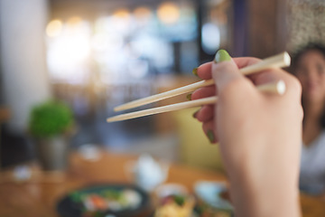 Image showing Tradition, bamboo chopsticks and hand of a person eating Japanese food at a restaurant for nutrition. Closeup of a woman with wooden sticks or utensil for dining, culture and cuisine for diet