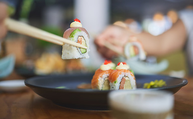 Image showing Chopsticks, food and eating sushi at a restaurant for nutrition at table. Closeup of hungry people with wooden sticks and soy sauce for dining, Japanese culture and cuisine with creativity on a plate