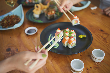 Image showing Sushi, hands and eating food with chopsticks at restaurant for nutrition at table. Closeup of people with wooden sticks for dining, Japanese culture and cuisine while sharing with creativity on plate