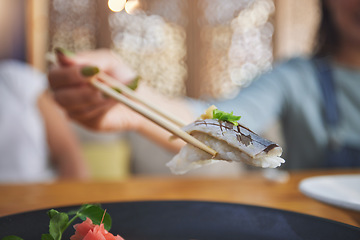 Image showing Food, hand and eating sushi with chopsticks at restaurant for nutrition and health. Closeup of a hungry person with wooden sticks for dining, Japanese culture and cuisine with creativity on fish