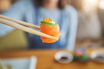 Image showing Sushi, eating food and hand with chopsticks at restaurant for nutrition and health. Closeup of a person with wooden sticks for dining, Japanese culture and salmon cuisine with creativity on fish