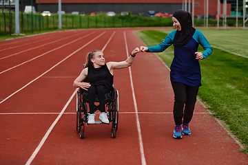 Image showing A Muslim woman wearing a burqa supports her friend with disability in a wheelchair as they train together on a marathon course.