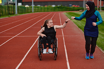 Image showing A Muslim woman wearing a burqa supports her friend with disability in a wheelchair as they train together on a marathon course.