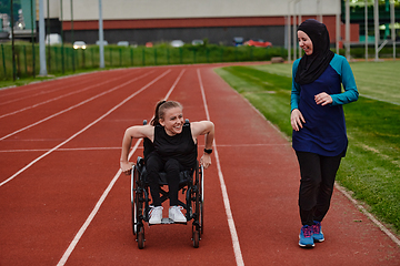 Image showing A Muslim woman in a burqa running together with a woman in a wheelchair on the marathon course, preparing for future competitions.