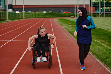 Image showing A Muslim woman in a burqa running together with a woman in a wheelchair on the marathon course, preparing for future competitions.