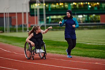 Image showing A Muslim woman wearing a burqa supports her friend with disability in a wheelchair as they train together on a marathon course.