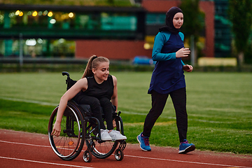 Image showing A Muslim woman wearing a burqa supports her friend with disability in a wheelchair as they train together on a marathon course.