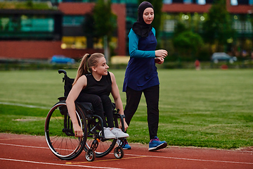 Image showing A Muslim woman in a burqa running together with a woman in a wheelchair on the marathon course, preparing for future competitions.