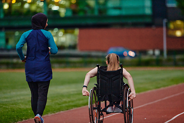 Image showing A Muslim woman in a burqa running together with a woman in a wheelchair on the marathon course, preparing for future competitions.