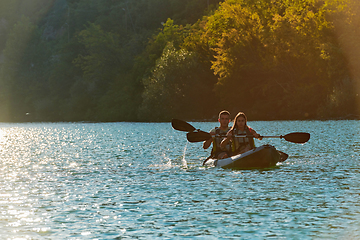 Image showing A young couple enjoying an idyllic kayak ride in the middle of a beautiful river surrounded by forest greenery in sunset time