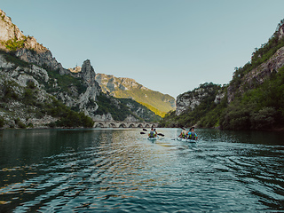 Image showing A group of friends enjoying having fun and kayaking while exploring the calm river, surrounding forest and large natural river canyons