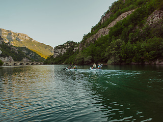 Image showing A group of friends enjoying having fun and kayaking while exploring the calm river, surrounding forest and large natural river canyons