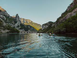 Image showing A group of friends enjoying having fun and kayaking while exploring the calm river, surrounding forest and large natural river canyons