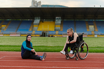 Image showing Two strong and inspiring women, one a Muslim wearing a burka and the other in a wheelchair stretching and preparing their bodies for a marathon race on the track