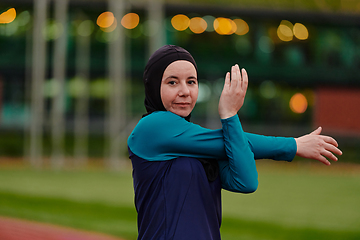 Image showing A Muslim woman in a burqa, an Islamic sports outfit, is doing body exercises, stretching her neck, legs and back after a hard training session on the marathon course.