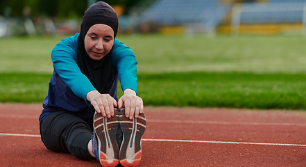 Image showing A Muslim woman in a burqa, an Islamic sports outfit, is doing body exercises, stretching her neck, legs and back after a hard training session on the marathon course.