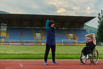 Image showing Two strong and inspiring women, one a Muslim wearing a burka and the other in a wheelchair stretching and preparing their bodies for a marathon race on the track