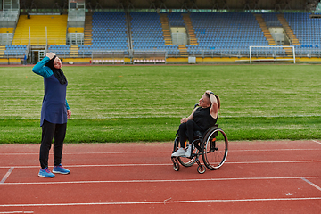 Image showing Two strong and inspiring women, one Muslim in a burka and the other in a wheelchair stretching necks while on the marathon course