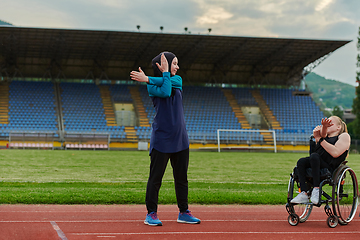 Image showing Two strong and inspiring women, one a Muslim wearing a burka and the other in a wheelchair stretching and preparing their bodies for a marathon race on the track