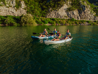 Image showing A group of friends enjoying fun and kayaking exploring the calm river, surrounding forest and large natural river canyons during an idyllic sunset.