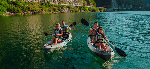 Image showing A group of friends enjoying fun and kayaking exploring the calm river, surrounding forest and large natural river canyons during an idyllic sunset.