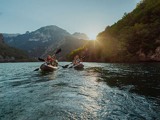 Image showing A group of friends enjoying fun and kayaking exploring the calm river, surrounding forest and large natural river canyons during an idyllic sunset.