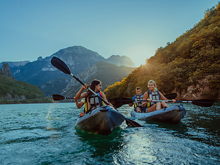 Image showing A group of friends enjoying fun and kayaking exploring the calm river, surrounding forest and large natural river canyons during an idyllic sunset.