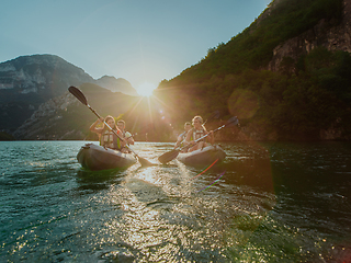 Image showing A group of friends enjoying fun and kayaking exploring the calm river, surrounding forest and large natural river canyons during an idyllic sunset.