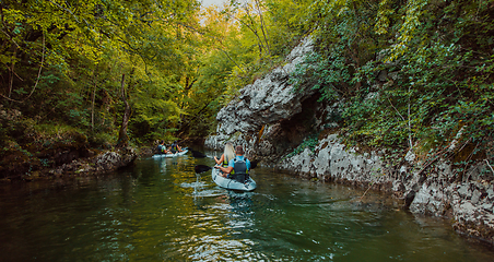 Image showing A group of friends enjoying having fun and kayaking while exploring the calm river, surrounding forest and large natural river canyons