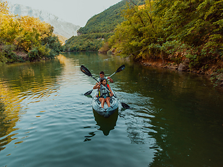 Image showing A group of friends enjoying fun and kayaking exploring the calm river, surrounding forest and large natural river canyons during an idyllic sunset.