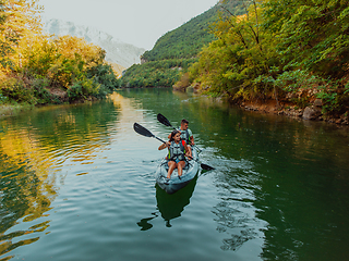 Image showing A group of friends enjoying fun and kayaking exploring the calm river, surrounding forest and large natural river canyons during an idyllic sunset.