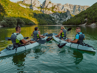 Image showing A group of friends enjoying having fun and kayaking while exploring the calm river, surrounding forest and large natural river canyons