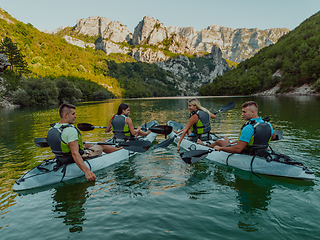 Image showing A group of friends enjoying having fun and kayaking while exploring the calm river, surrounding forest and large natural river canyons