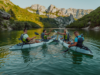 Image showing A group of friends enjoying having fun and kayaking while exploring the calm river, surrounding forest and large natural river canyons