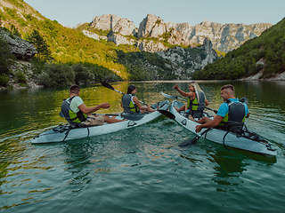 Image showing A group of friends enjoying having fun and kayaking while exploring the calm river, surrounding forest and large natural river canyons