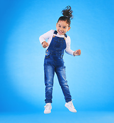 Image showing Happy, jumping and portrait of a child in a studio with excitement, joy or wow expression. Happiness, smile and full length of a girl kid model moving for good news isolated by a blue background.