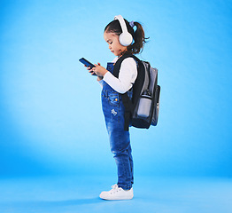 Image showing Headphones, backpack and child on blue background with phone ready for school, learning and education. Kindergarten, and young girl with bag on smartphone for streaming music, audio and radio