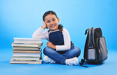 Image showing Girl child, sitting and books in studio portrait, backpack and excited for learning on floor by blue background. Female kid, education and development with smile, future and studying for knowledge