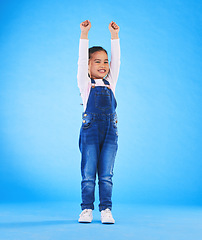 Image showing Celebration, girl child and champion, winner and achievement with happiness and excited isolated on blue background. Cheers, yes and winning with success, pride and happy kid with arms up in a studio