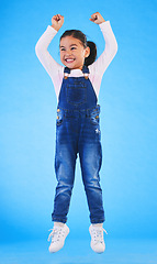 Image showing Girl child, jump and celebration in studio with fist in air for goal, achievement or success by blue background. Female kid, excited winner and champion with yes, energy or motivation for competition