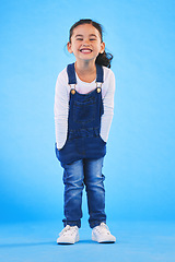 Image showing Excited girl child, fashion and studio portrait with jeans, dungaree and trendy style by blue background. Female kid model, smile and happy for clothes, aesthetic and youth culture by backdrop