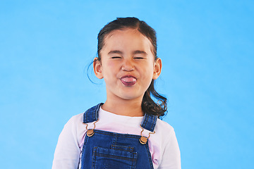 Image showing Funny, face of child and girl with silly, goofy or facial expression on blue background in studio with fashion for children. Kid, portrait and tongue out of mouth in joke, humor or emoji for comedy