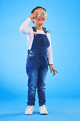 Image showing Girl child, glasses and smile in studio with vision, health and thinking for eye care by blue background. Female kid, test spectacles and young fashion model with lens, frame and excited for wellness