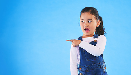 Image showing Pointing, blue background and girl with mockup space for sale, advertising and promotion. Emoji, happy and young child in studio with hand gesture for discount information, announcement and news