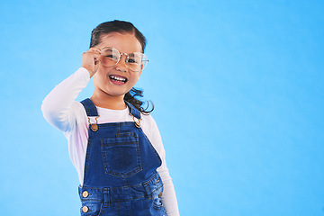 Image showing Girl child, glasses and frame in studio portrait for vision, health and eye care by blue background. Female kid, test spectacles and young fashion model with lens, smile or eyesight with mockup space