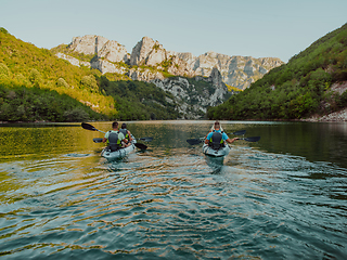 Image showing A group of friends enjoying having fun and kayaking while exploring the calm river, surrounding forest and large natural river canyons