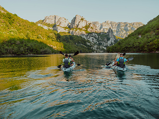 Image showing A group of friends enjoying having fun and kayaking while exploring the calm river, surrounding forest and large natural river canyons